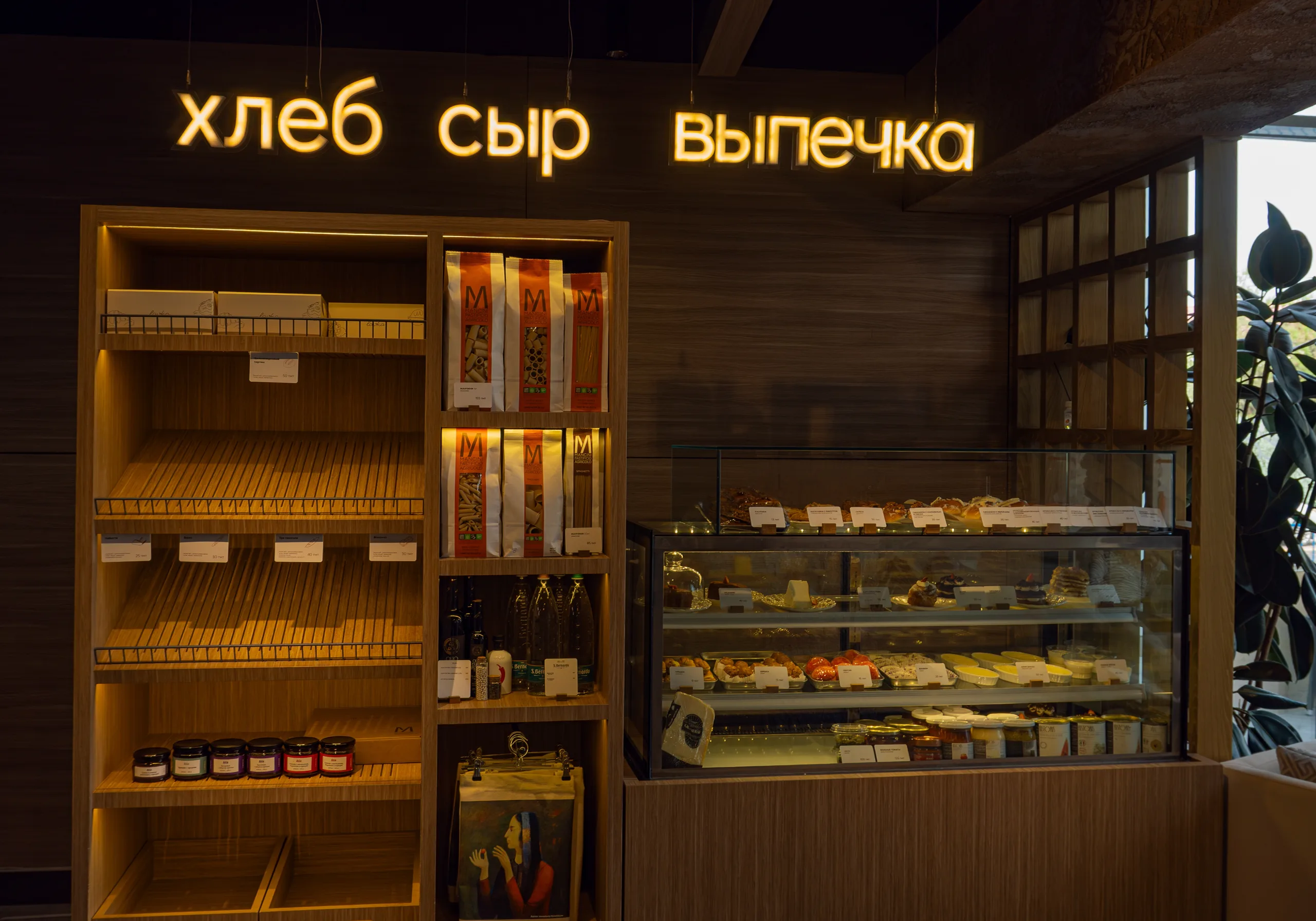 Витрина с десертами и деревянные полки под жёлтой неоновой надписью «хлеб сыр выпечка» в тёплом свете кафе Lavka.