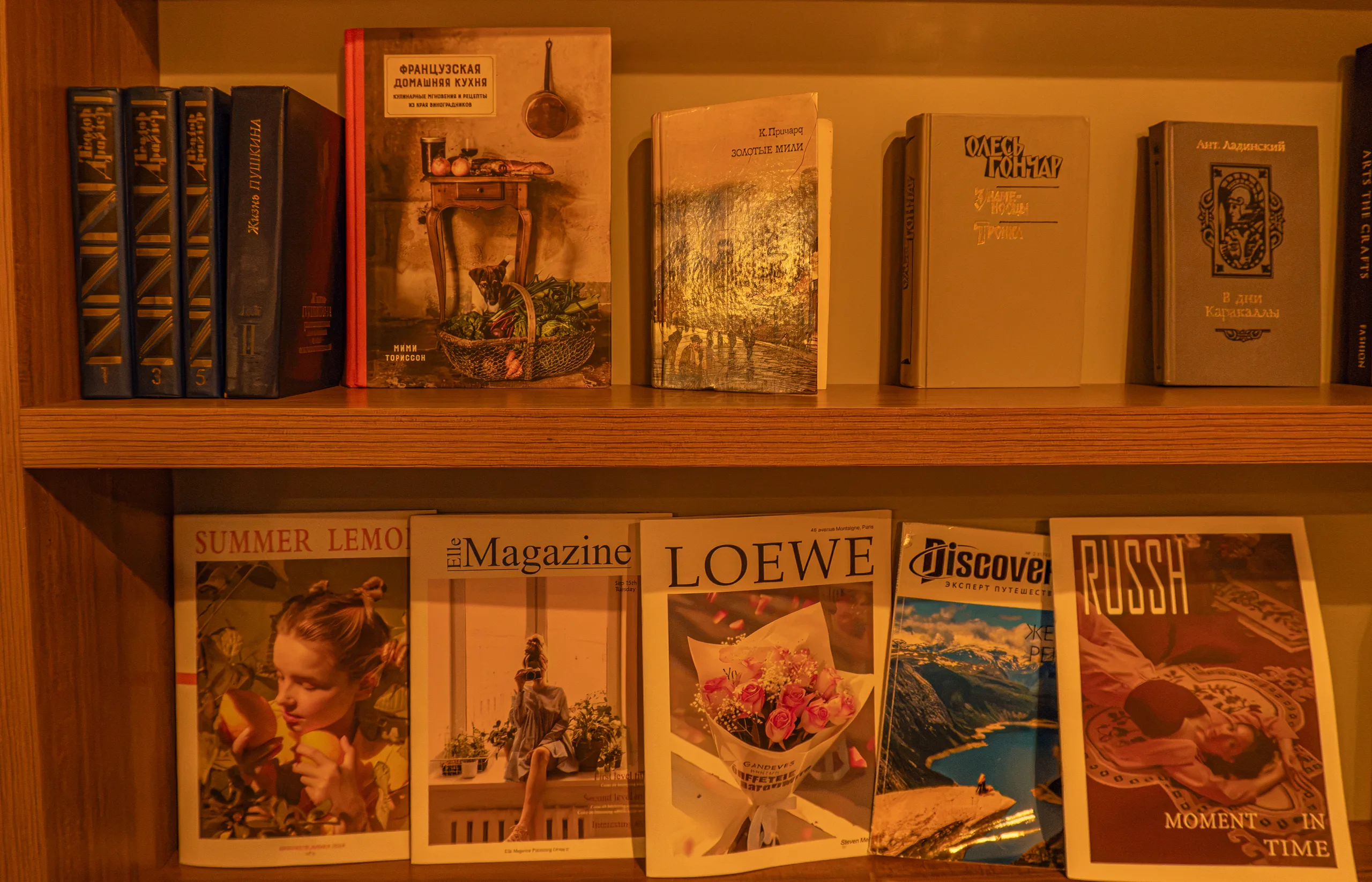 Книжная полка с книгами и глянцевыми журналами в тёплом свете.